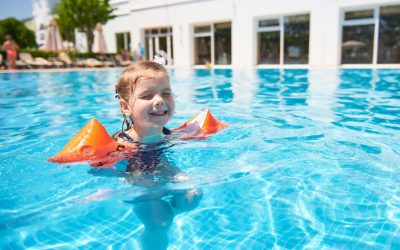 Girl swimming in the pool in armlets on a hot summer day. Family vacation in a tropical resort